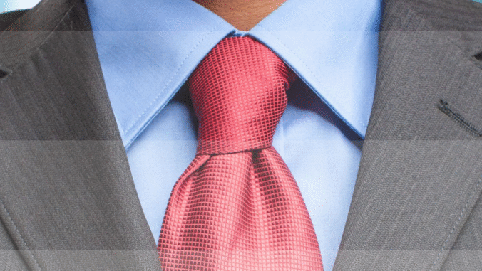 Close-up of a person wearing a light blue dress shirt, a red textured tie, and a gray suit jacket. The focus is on the knot of the tie and the collar of the shirt.