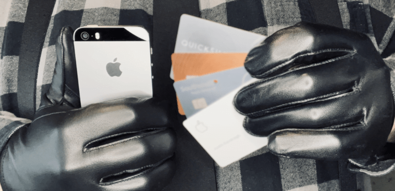 Man's black-leather gloved hands holding a cell phone in the right hand and four credit cards in the left hand
