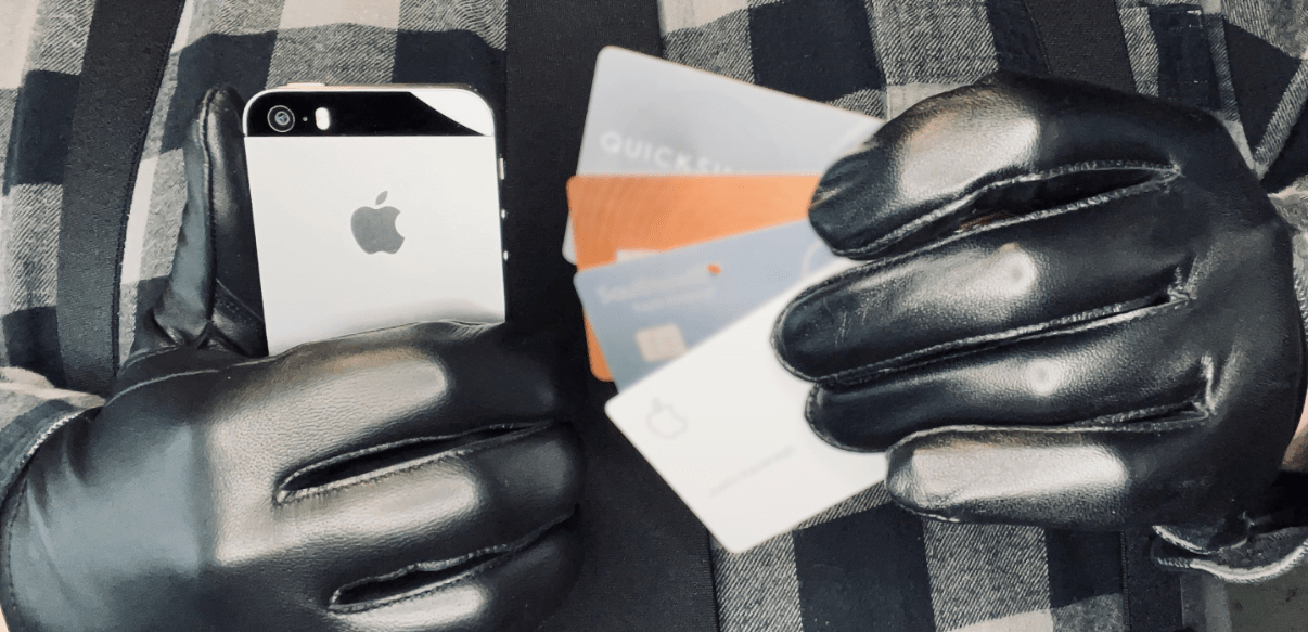 Man's black-leather gloved hands holding a cell phone in the right hand and four credit cards in the left hand
