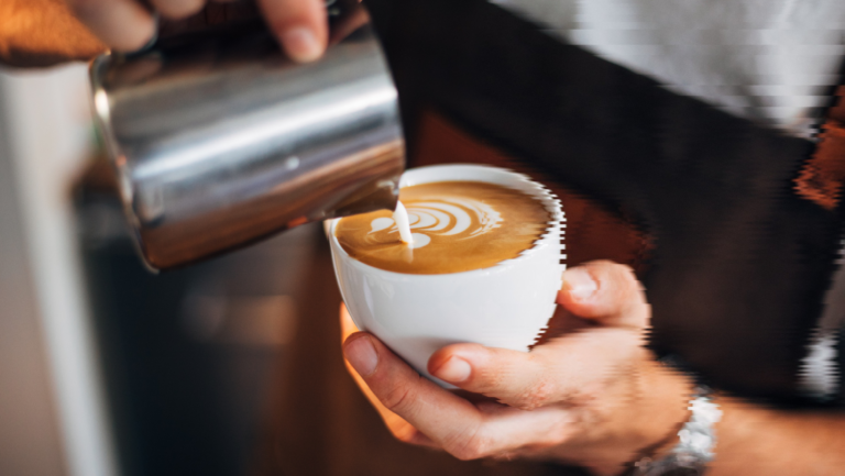 A barista pouring milk into a cup of coffee, creating latte art.