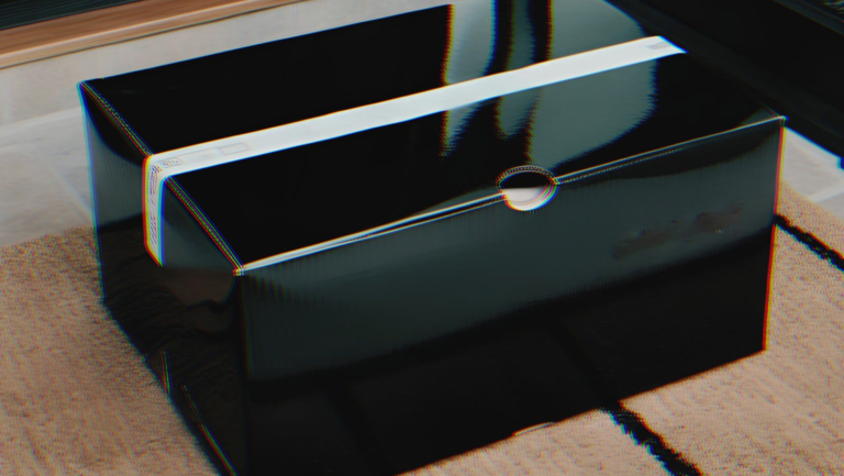 A glossy black shoe box with a thin white stripe across the middle, placed on a textured beige surface.