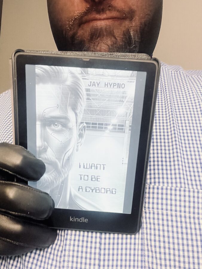 Jay Hypno holding up His Kindle e-reader with “I Want to Be a Cyborg” cover on the screen