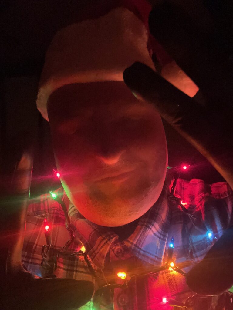 Jay Hypno in a stocking mask and Santa hat with festive Christmas lights around His neck.