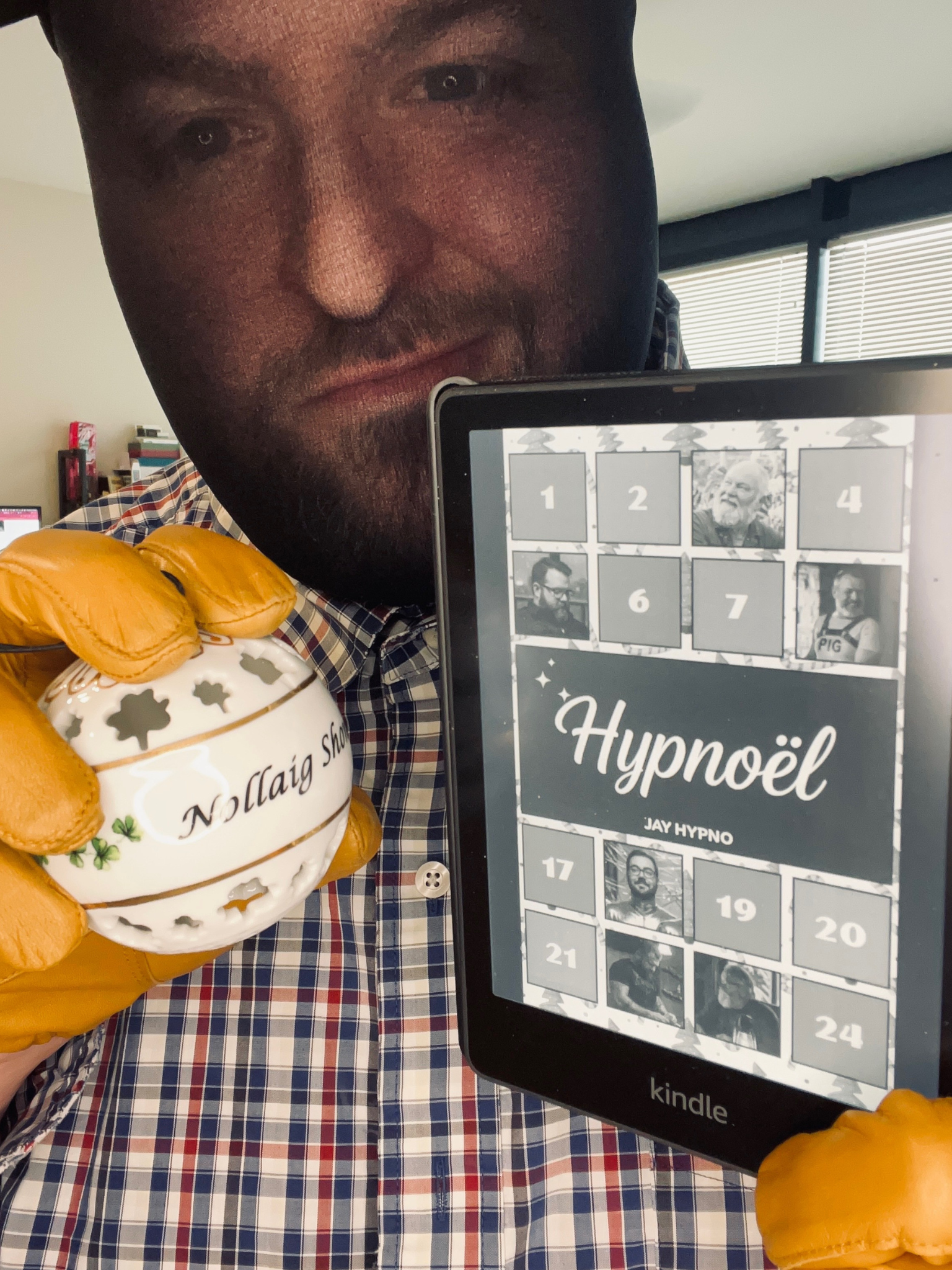 Jay Hypno wearing tan gloves holds a decorative ornament and a Kindle displaying a digital book titled Hypnoël.